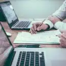 person holding pencil near laptop computer