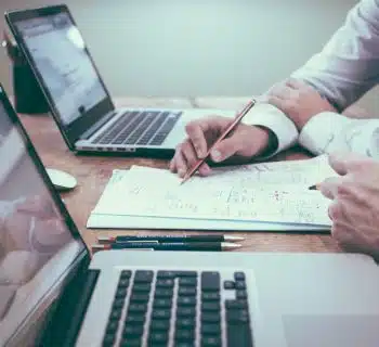 person holding pencil near laptop computer